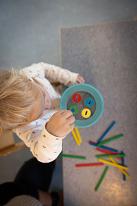 Ett barn övar sin motorik på förskolan genom att som stoppar färgade föremål i en hink