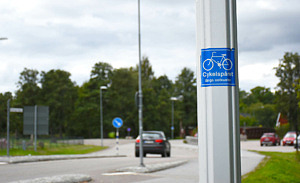 Närbild på stolpe med ett klistermärke med en cykel och texten Cykelspåret längs ostkusten, i bakgrunden en bil som kör bort