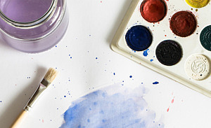 Bild på ett vitt papper med en pensel, en burk vatten och vattenfärg.