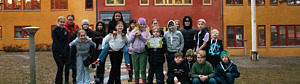 Elever står i en klunga på skolgården med skolbyggnad i bakgrunden, en elev håller i ett diplom och en annan en pokal i guld