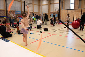 Flicka syns dansa med pinnar med färgglada tygbitar, i bakgrunden syns flera barn leka med olika redskap.