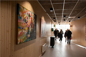 I förgrunden skymtar två färgglada konstverk, i bakgrunden syns människor gå bortåt och hallen bli mindre.