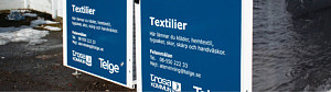 Insamlingskärl med blå dekal och vit text, Textilier, Trosa kommuns och Telge Återvinnings logotyper