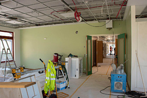 Rum under byggnation med ljusgröna väggar, byggmaskiner på golvet och en korridor som leder till entré.