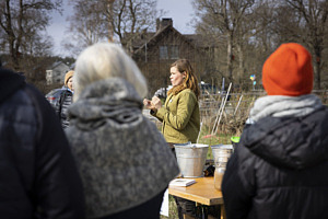 Ett flertal personer står och lyssnar till Hanna Hofman-Bang som berättar om jord och kompost.