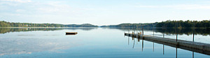 Sjön Sillen ligger spegelblank, en brygga som leder ut på vattnet syns till höger i bild