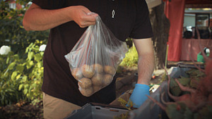 Torghandlare plockar ihop potatis från bord med grönsaker.