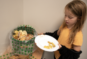 Flicka håller en tallrik med matrester vid en avfallshink.