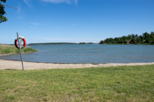 Badplatsen Borgmästarholmen. Gräs i förgrunden, följt av sandstrand därefter hav och i bakgrunden öar.