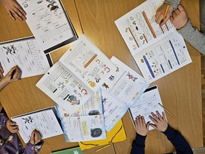 Inomhus, a4-papper på ett bord, händer med pennor som skriver.