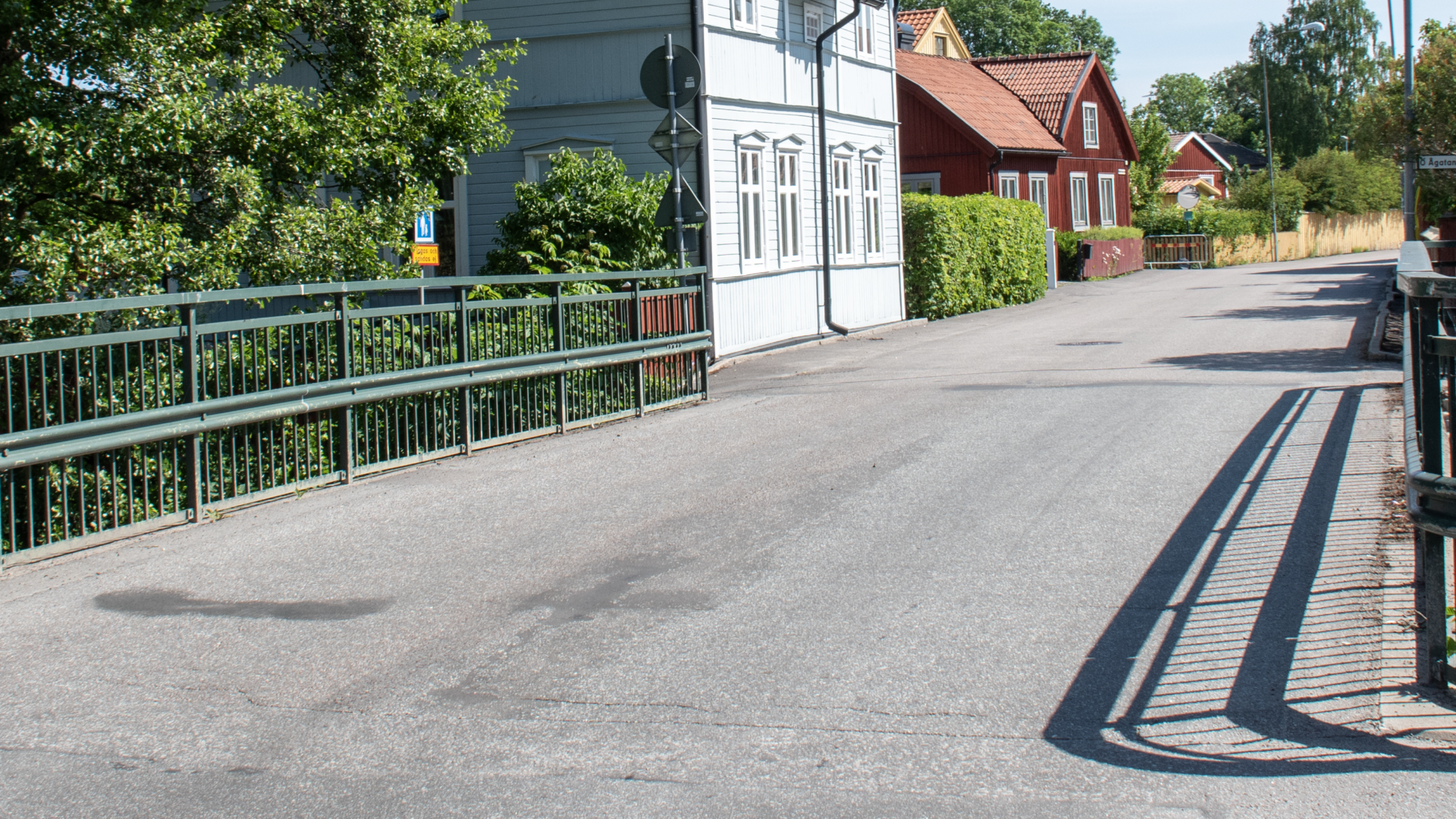 Utomhus, en väg med räcken längs med sidorna, hus i bakgrunden.