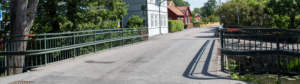 Utomhus, en väg med räcken längs med sidorna, hus i bakgrunden.