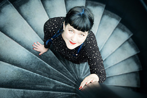 Kvinna fotograferad ovanifrån i ett runt trapphus. Hon tittar rakt upp i kameran, runt omkring syns trapporna.