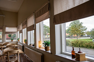 Matsal med bord och stolar till vänster och fönster med gardiner och dekorationer på fönsterbrädan.