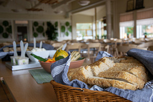 Ett bord i förgrunden med bröd, bakom byttor med smör och därefter bord och stolar.